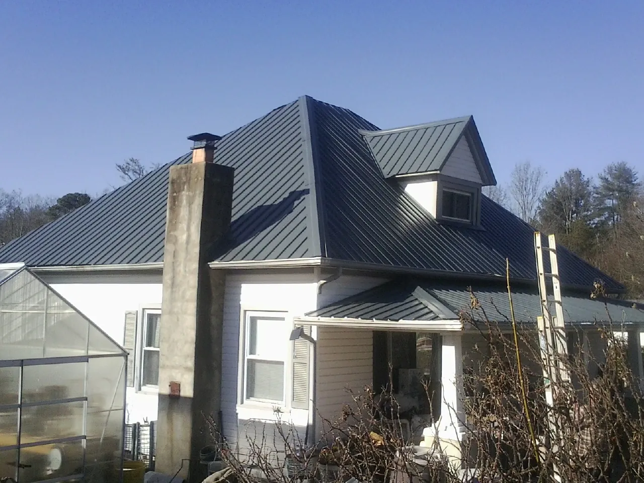 Dark blue standing seam metal roof on a white farmhouse with dormer — Slate & Tile Roof Repair by Roofing Brothers in Woonsocket