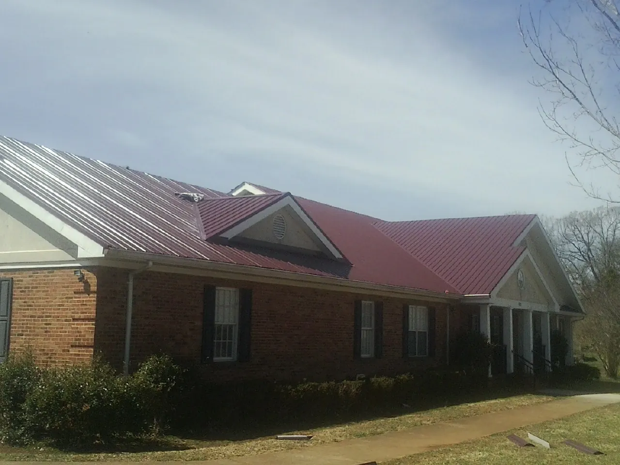 Red metal roof with gabled entries on a long brick building, from a Hail Damage Roof Repair job in Woonsocket