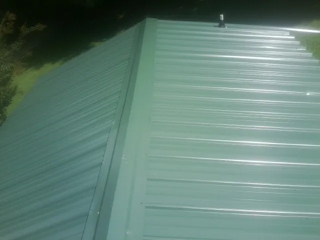New green metal panels meeting at the ridge of a roof — Flat Roof Repair work by our crew in Woonsocket