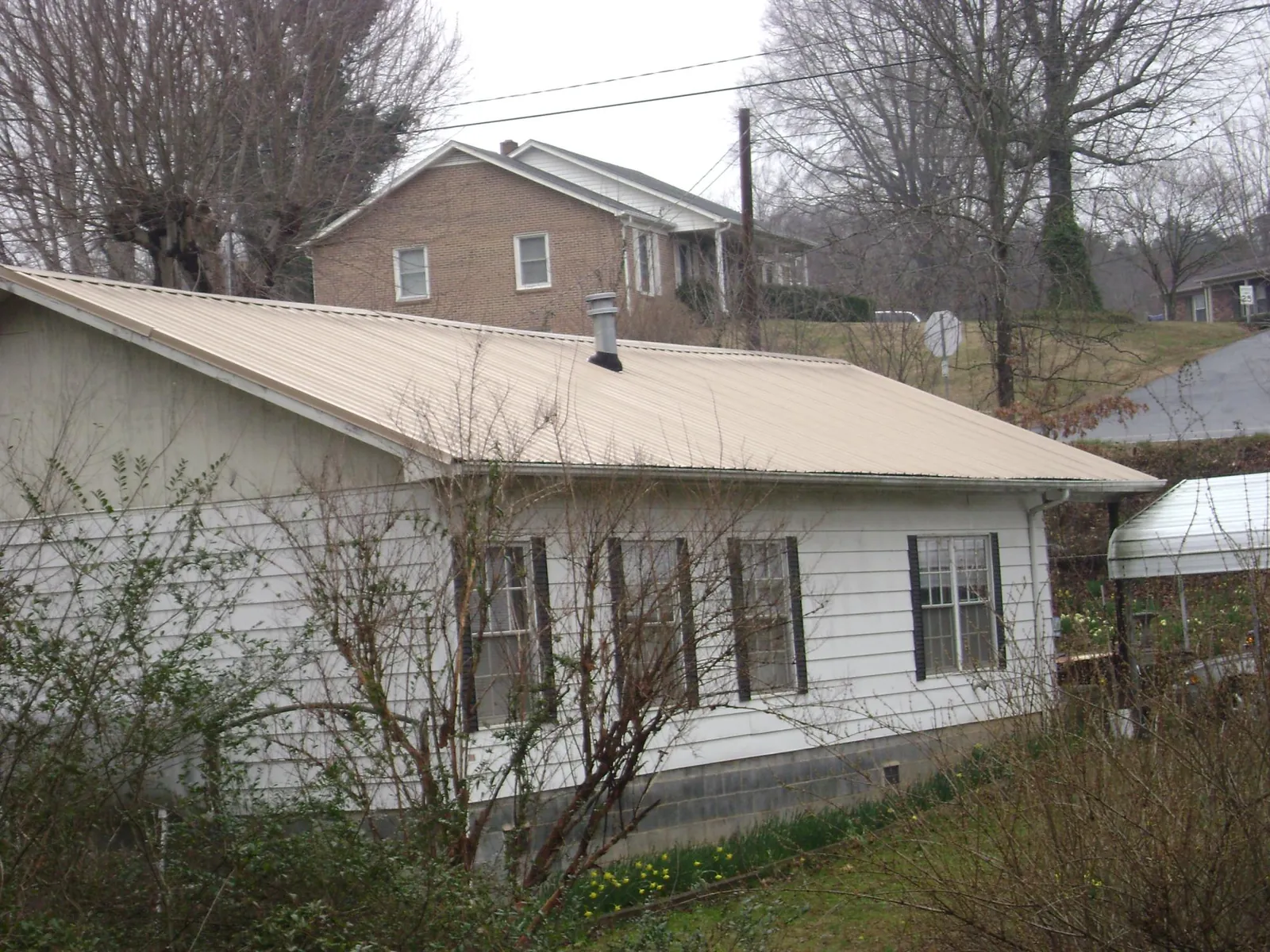 Tan metal roof on a white sided house set into a hillside — Commercial Roofing by Roofing Brothers in Woonsocket